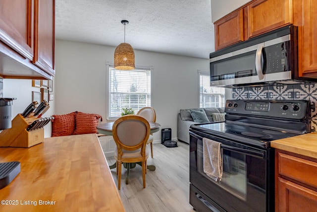 kitchen featuring black / electric stove, wooden counters, light wood-type flooring, and pendant lighting