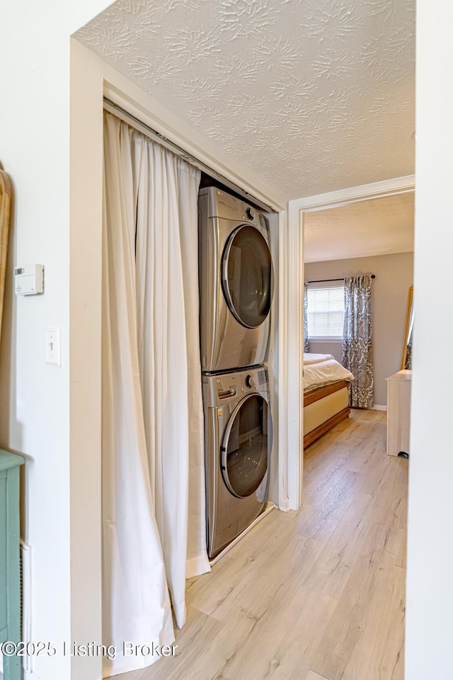 clothes washing area with stacked washing maching and dryer, a textured ceiling, and light hardwood / wood-style flooring