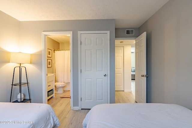 bedroom with connected bathroom, a textured ceiling, and light hardwood / wood-style floors