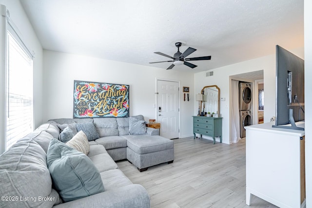 living room featuring ceiling fan, stacked washing maching and dryer, light hardwood / wood-style floors, and a textured ceiling