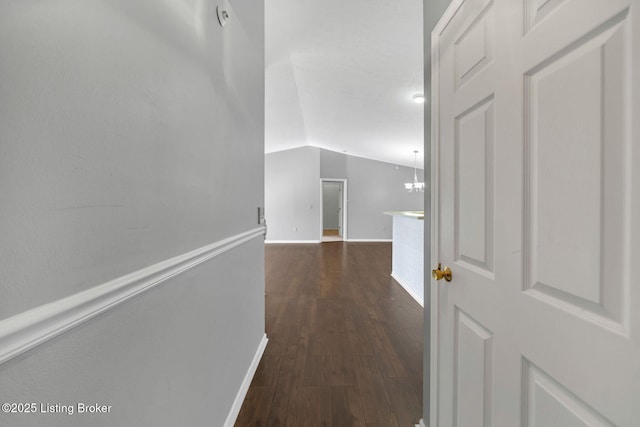 corridor with an inviting chandelier, dark wood-type flooring, and vaulted ceiling