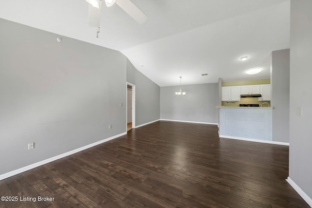 unfurnished living room with vaulted ceiling, dark wood-type flooring, and ceiling fan with notable chandelier