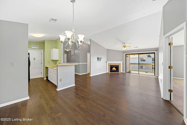 kitchen featuring sink, decorative light fixtures, vaulted ceiling, a tiled fireplace, and white cabinets