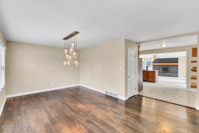 unfurnished room with a brick fireplace, ceiling fan with notable chandelier, and light hardwood / wood-style floors