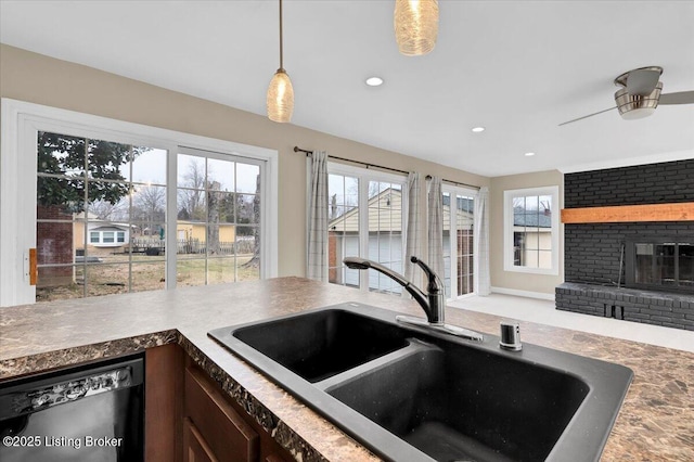 kitchen featuring sink, ceiling fan, dishwasher, hanging light fixtures, and a brick fireplace