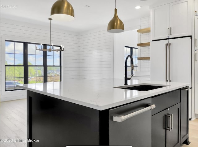 kitchen with sink, light stone counters, hanging light fixtures, stainless steel dishwasher, and white cabinets