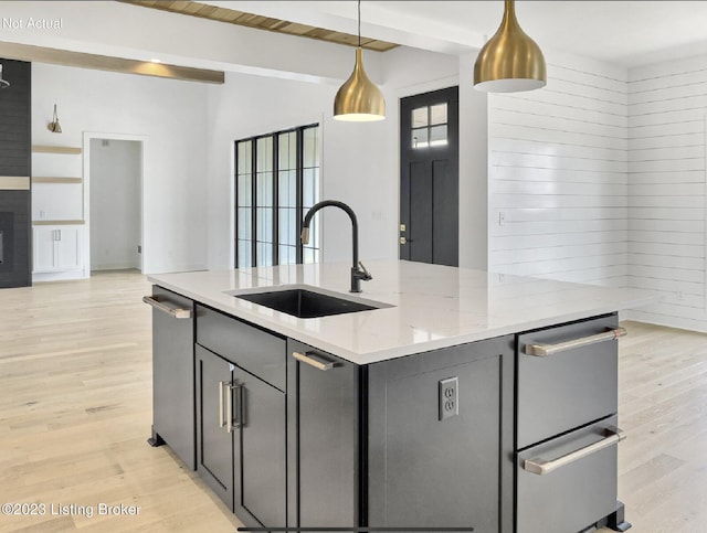 kitchen with light stone counters, sink, hanging light fixtures, and light wood-type flooring