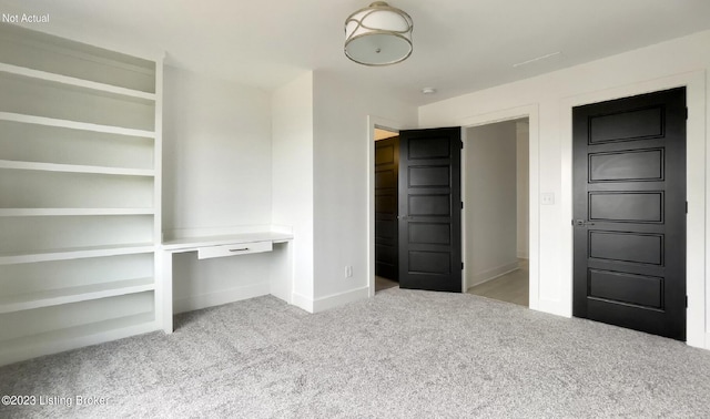 unfurnished bedroom featuring light colored carpet and built in desk