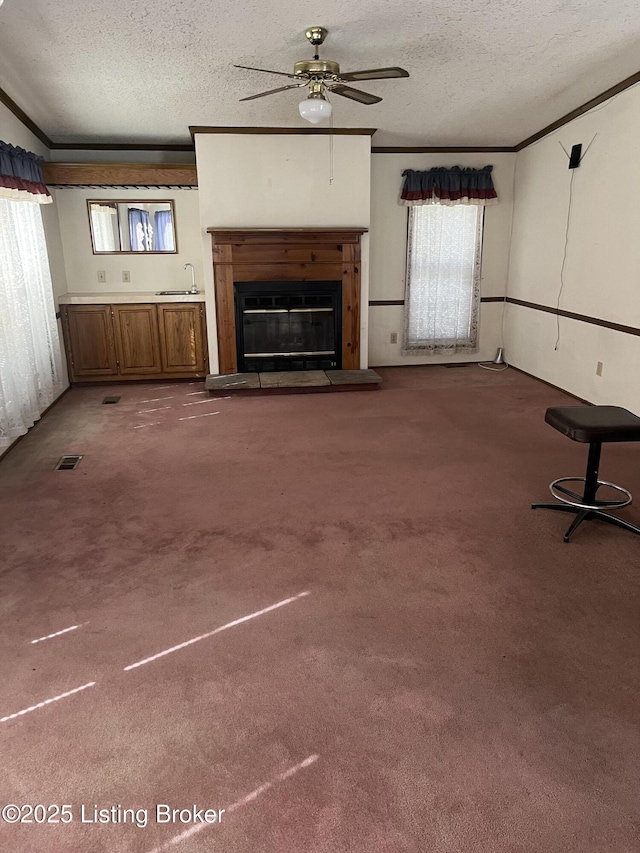 unfurnished living room with ornamental molding, carpet, sink, and a textured ceiling