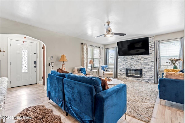 living room with ceiling fan, a stone fireplace, and light hardwood / wood-style floors