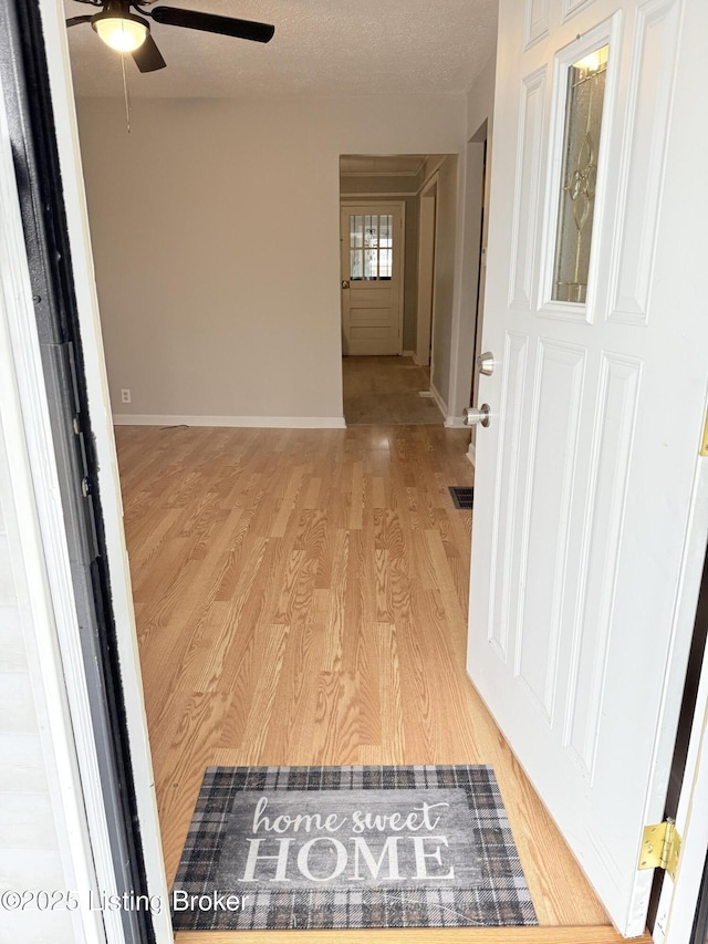 hall with light wood finished floors, visible vents, baseboards, and a textured ceiling