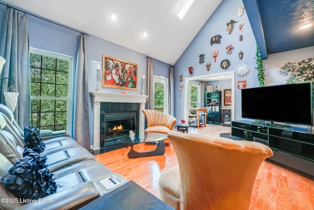 living room featuring high vaulted ceiling, a tiled fireplace, and hardwood / wood-style floors