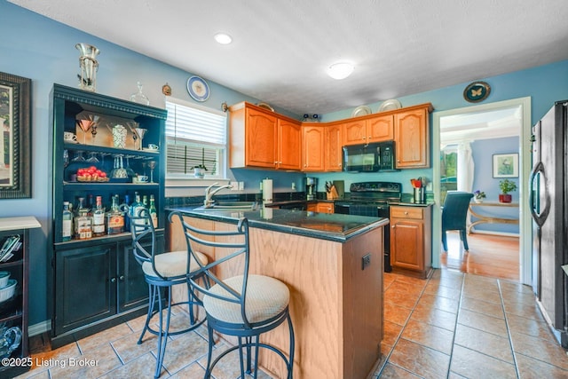 kitchen featuring sink, light tile patterned floors, a kitchen breakfast bar, a kitchen island, and black appliances