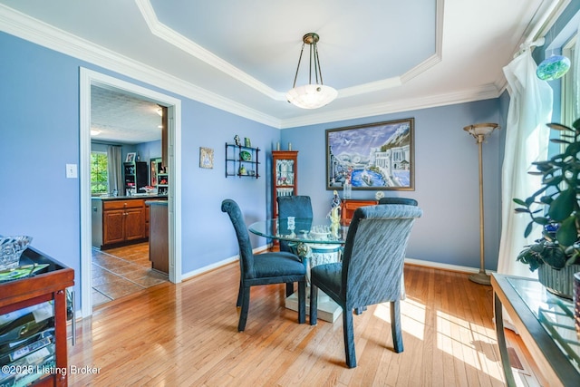 dining space featuring crown molding, a tray ceiling, and light wood-type flooring