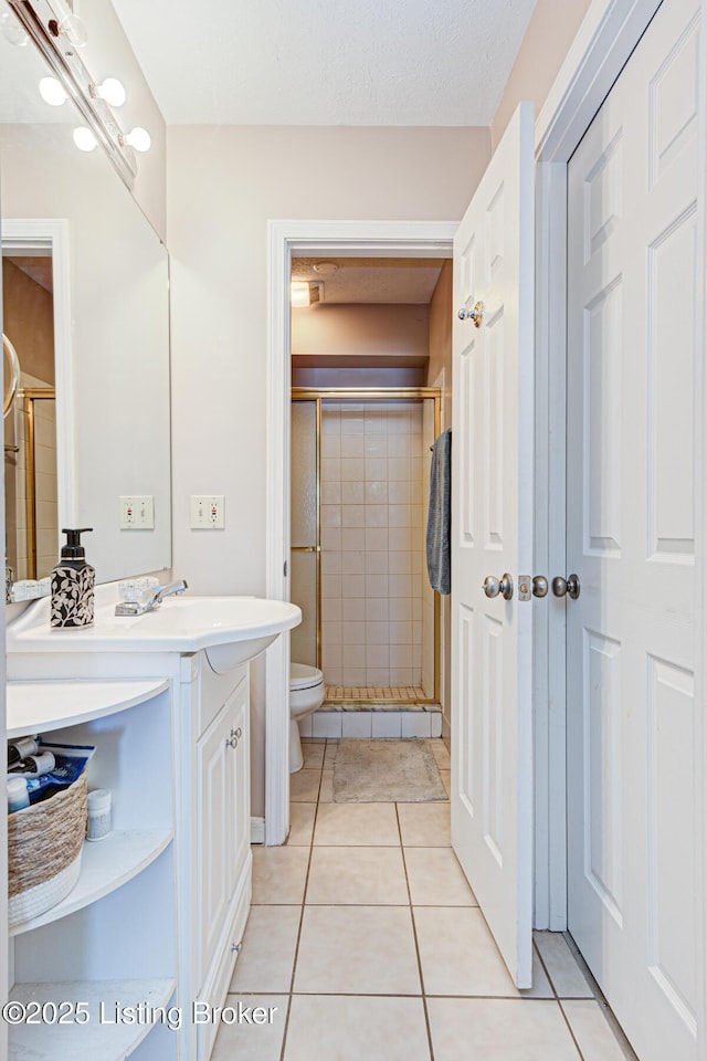 bathroom with a shower with shower door, tile patterned flooring, vanity, toilet, and a textured ceiling