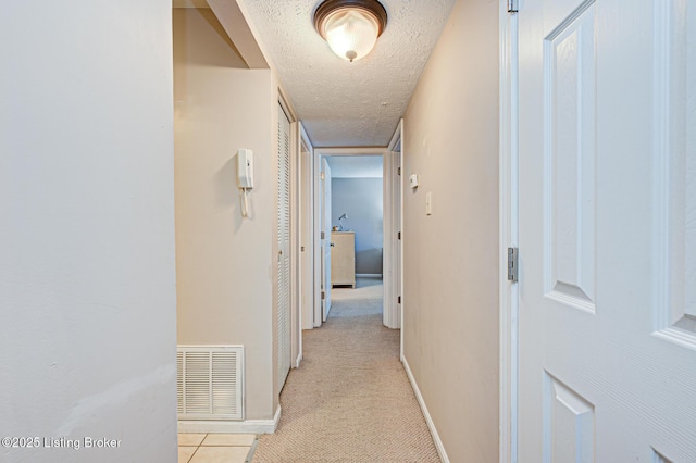 hallway with light colored carpet and a textured ceiling