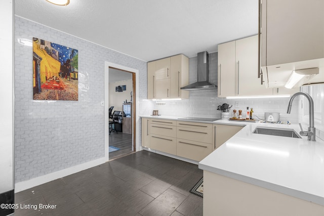 kitchen with wall chimney range hood, sink, black electric stovetop, decorative backsplash, and cream cabinetry