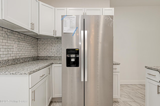 kitchen featuring white cabinetry, stainless steel fridge, light stone counters, and backsplash