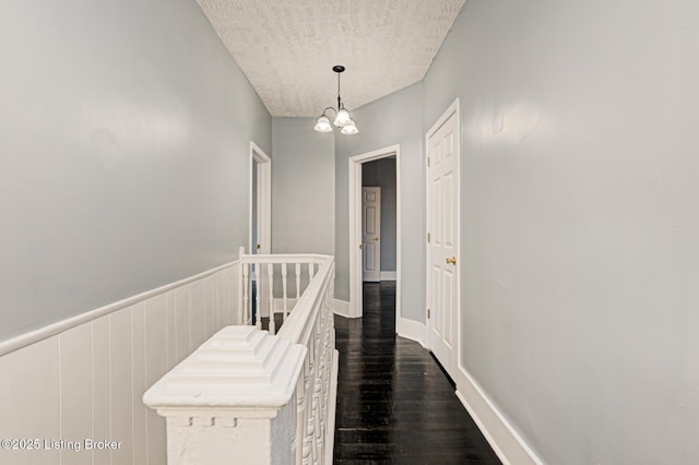 corridor with dark hardwood / wood-style flooring, a chandelier, and a textured ceiling