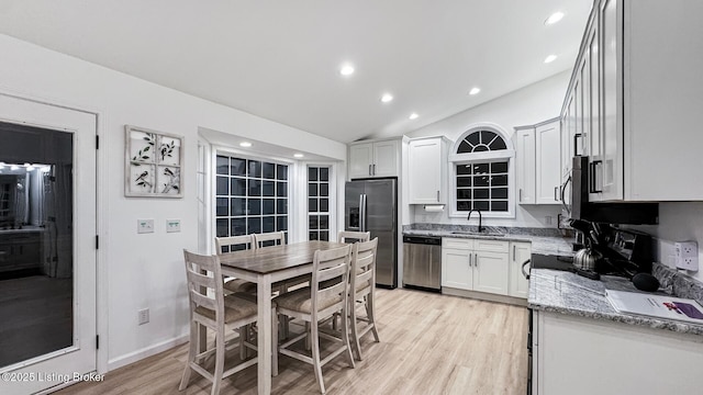 kitchen with sink, appliances with stainless steel finishes, light stone counters, white cabinets, and light wood-type flooring