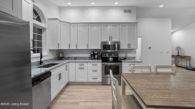 kitchen with sink, light stone counters, light hardwood / wood-style flooring, appliances with stainless steel finishes, and white cabinets