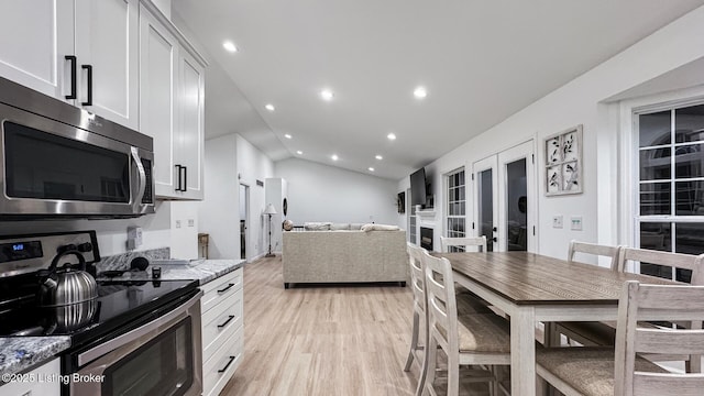 kitchen with stainless steel appliances, white cabinetry, light stone countertops, and light wood-type flooring