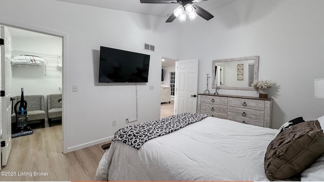 bedroom featuring lofted ceiling, a spacious closet, light wood-type flooring, a closet, and ceiling fan