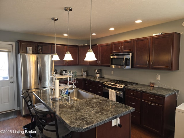 kitchen featuring hanging light fixtures, an island with sink, appliances with stainless steel finishes, and a kitchen bar