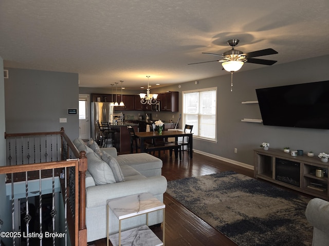 living room featuring a textured ceiling, dark wood-type flooring, a healthy amount of sunlight, and ceiling fan with notable chandelier