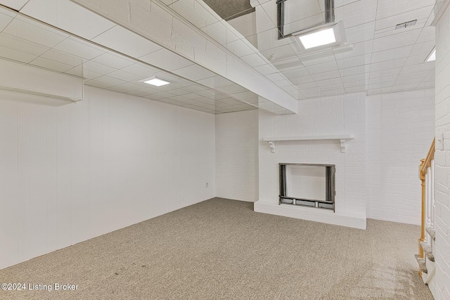 basement featuring a fireplace, carpet floors, brick wall, and a paneled ceiling