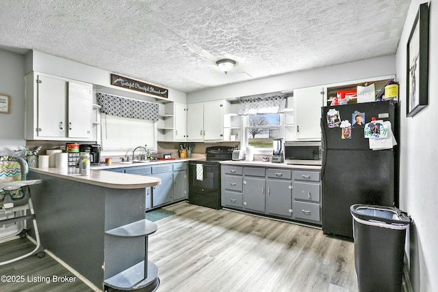 kitchen featuring black appliances, gray cabinetry, white cabinets, light hardwood / wood-style floors, and kitchen peninsula