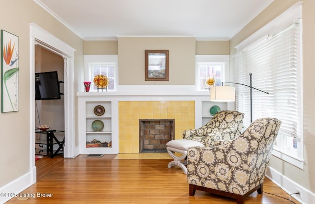 living area featuring crown molding, wood-type flooring, a tiled fireplace, and built in features