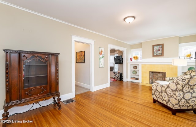 sitting room with a tiled fireplace, crown molding, and light hardwood / wood-style floors