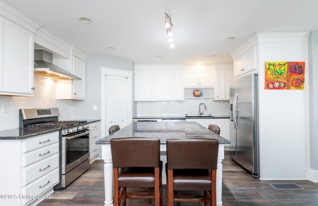 kitchen with sink, white cabinetry, dark stone countertops, appliances with stainless steel finishes, and wall chimney range hood