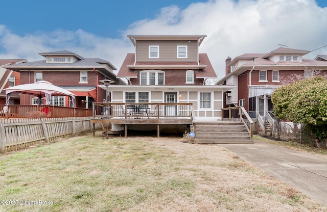 back of property featuring a wooden deck, a lawn, and a sunroom