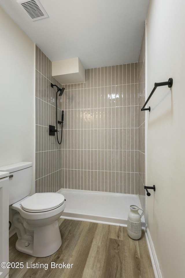 bathroom featuring tiled shower, wood-type flooring, and toilet