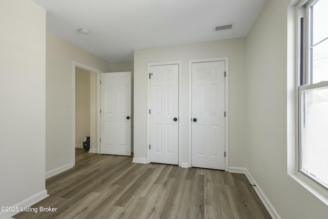 unfurnished bedroom with two closets and light hardwood / wood-style flooring