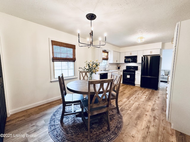 dining space with sink, a chandelier, a textured ceiling, and light hardwood / wood-style floors