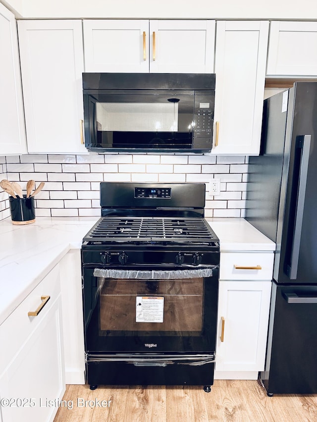 kitchen with light hardwood / wood-style flooring, backsplash, black appliances, light stone countertops, and white cabinets