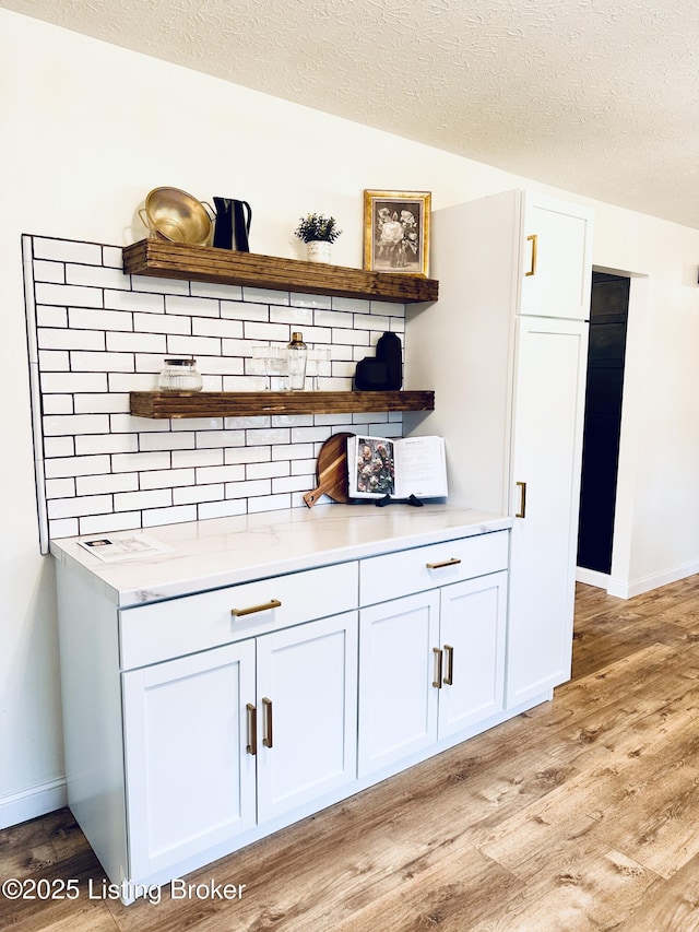 bar with tasteful backsplash, white cabinetry, and light hardwood / wood-style flooring