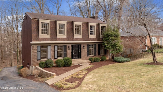 dutch colonial featuring brick siding, roof with shingles, a chimney, a gambrel roof, and a front yard