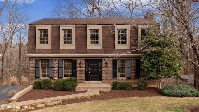 view of front of house with roof with shingles, a front yard, and brick siding