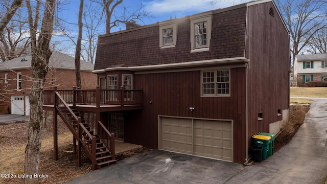 view of front facade featuring aphalt driveway, a chimney, stairway, a gambrel roof, and a deck