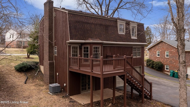 rear view of house with central AC unit, a gambrel roof, a chimney, stairway, and a wooden deck