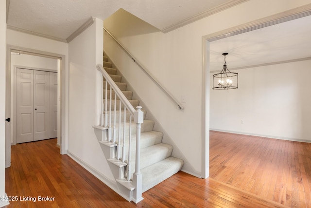 staircase with a notable chandelier, baseboards, crown molding, and wood finished floors