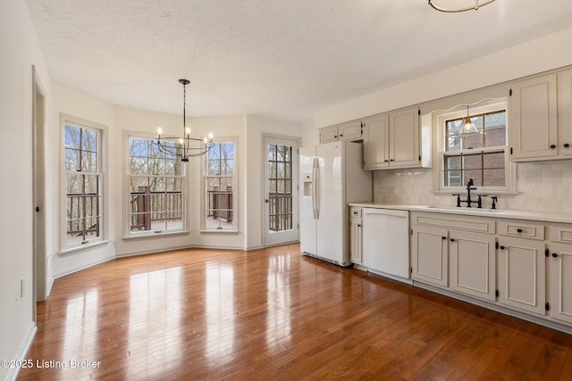 kitchen with decorative light fixtures, light countertops, a sink, wood finished floors, and white appliances