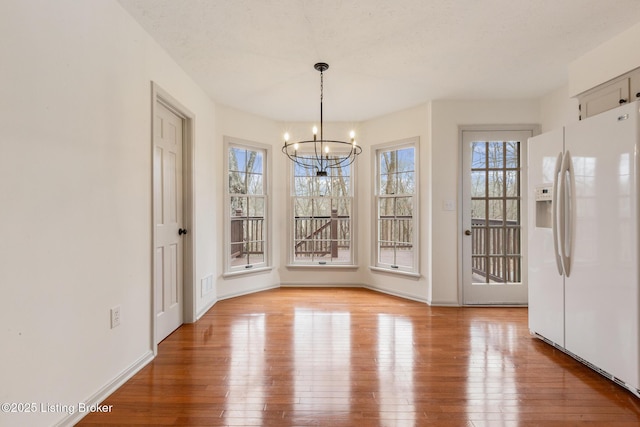 unfurnished dining area featuring light wood-style flooring, baseboards, and an inviting chandelier