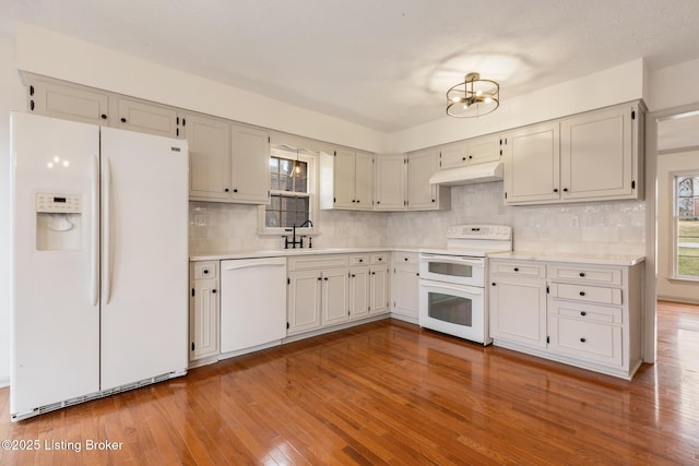 kitchen with light wood finished floors, light countertops, a sink, white appliances, and under cabinet range hood