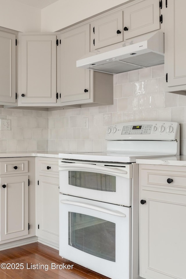 kitchen with range with two ovens, light countertops, decorative backsplash, white cabinetry, and under cabinet range hood