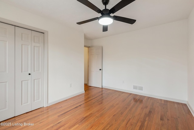 unfurnished bedroom with a closet, visible vents, ceiling fan, wood finished floors, and baseboards